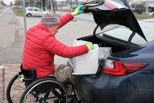 A man in a wheelchair takes a white bag out of the trunk of his car