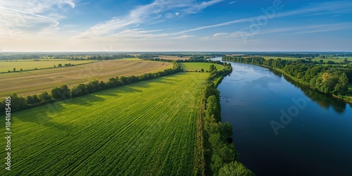 Fototapeta Naklejka Na Ścianę i Meble -  Aerial drone view of lush green meadows beside a river, suitable for background or layout design