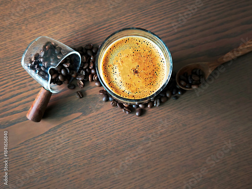 The hot coffee has crema and coffee beans on the wooden floor.