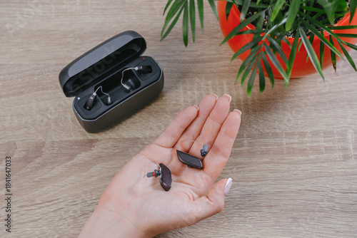 Close-up of female hands holding and showing a pair of modern digital hearing aids. Audiology clinic demonstration of advanced hearing technology. Top view