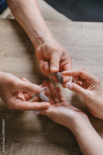 Close-up of audiologist giving modern hearing aid for patient in clinic. Hearing device demonstration with open case and earbud accessories.