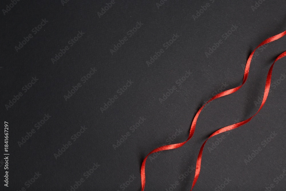 Naklejka premium Beautiful red ribbons on dark background, top view. Space for text