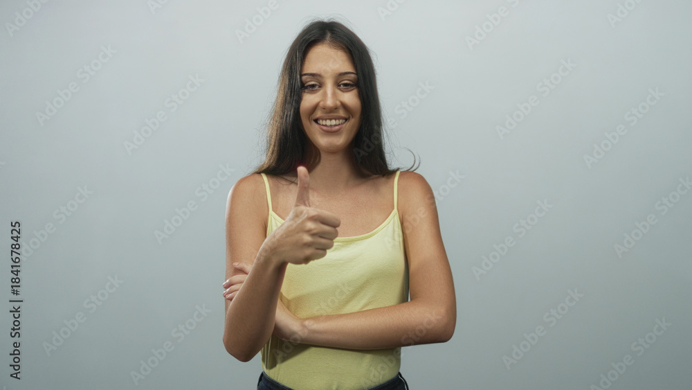 Obraz premium Young hispanic woman with arms crossed giving a thumbs up in a softly lit light gray studio; confidence.
