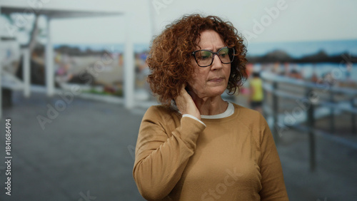 Foto Middle-aged woman with curly hair standing thoughtfully at the seaside with beach background wearing glasses and sweater outdoors in daylight