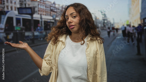 Young african american woman holds palm up on street at tram stop with casual t shirt and neutral gaze; indifference doubt.