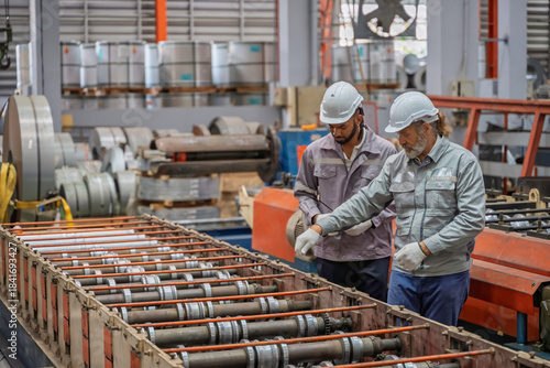 Two engineers wearing safety helmets and gloves operate a control panel in an industrial factory. Teamwork and safety procedures in modern manufacturing environment.