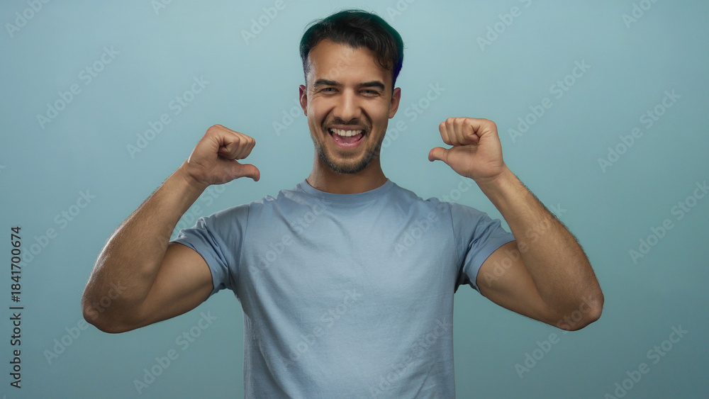 Fototapeta premium Hispanic man pointing at himself with thumbs over isolated blue background, expressing confidence and self-assurance in a casual setting.