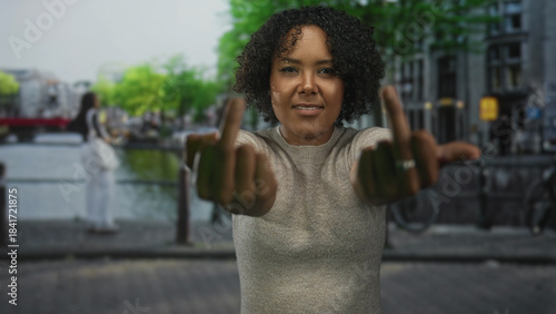 Tableau sur toile Woman flipping both middle fingers with extended arms on a canal city street outdoors; defiance attitude