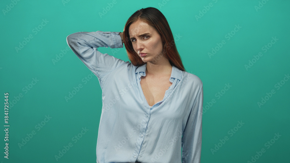 Fototapeta premium Redhead woman with hand behind head, furrowed brow, slightly exposed neckline and puzzled expression in studio; confusion.