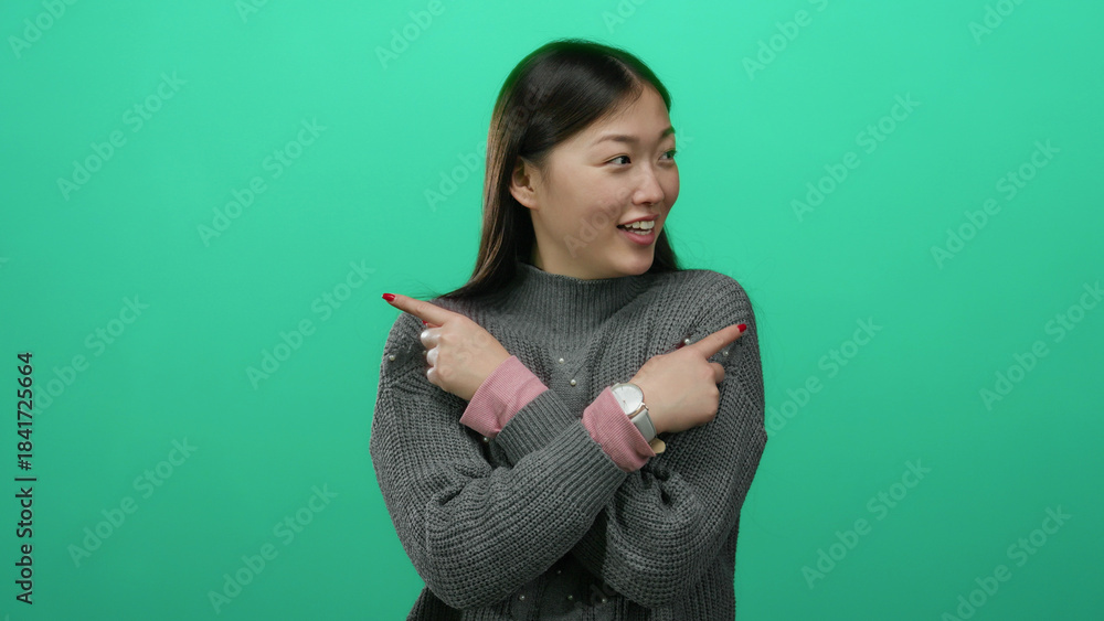 Obraz premium Woman smiling while pointing in opposite directions against vibrant green backdrop wearing cozy sweater and pink watch highlighting playful expression and modern style