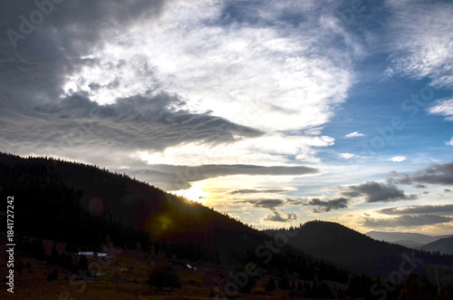 Tranquil mountain landscape at sunset with silhouetted trees and rolling hills, a distant ridge, and a warm sky. Golden light creates calm, peaceful atmosphere and natural beauty. Carpathian Mountains