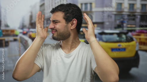 Fotografia Young hispanic man wearing white tshirt pressing hands to ear on busy construction site street; stress