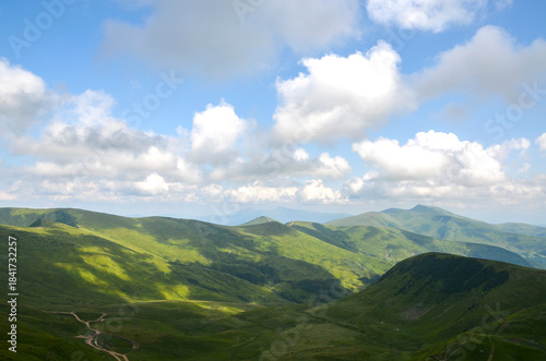 Tranquil panorama of grassy hills and distant mountains beneath partly cloudy sky. Warm light and soft shadows evoke peace, making this ideal for nature, travel, and landscape stock needs. Carpathians