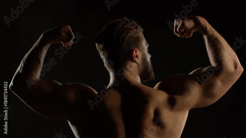 A bodybuilder poses against a black background