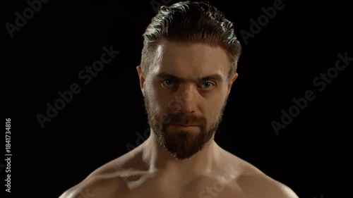 A bodybuilder enters the frame and looks at the camera against a black background