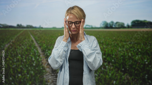 Fotografie Woman in glasses presses hands to temples in apparent headache then folds palms as if praying in a studio field scene; anxiety reflection