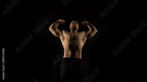 A bodybuilder poses against a black background