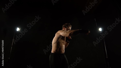 A muscular fighter is boxing with a shadow on a black background