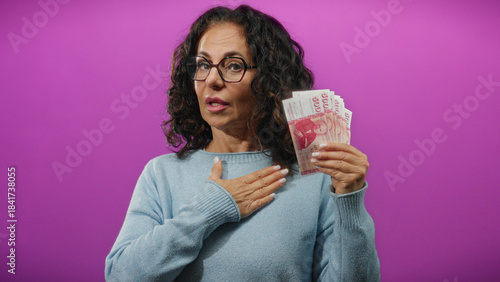 Schilderij op canvas Woman holding icelandic krona banknotes against a vibrant purple background, symbolizing financial commitment or promise