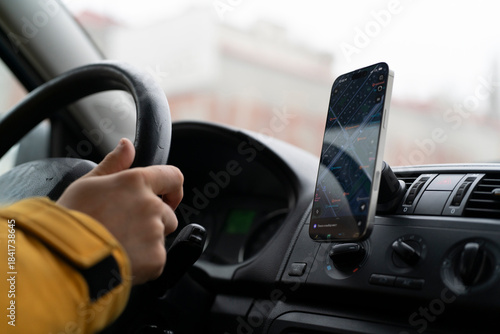 A person is driving a car while using a smartphone for directions. The car is in motion