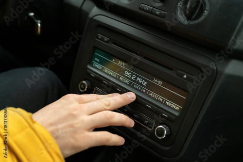 A person is tuning the radio in a car during a drive on a clear day