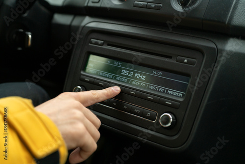 A person sits in a car and changes the radio to play their favorite station