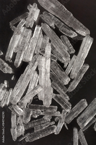 A pile of translucent, colorless menthol crystals is scattered on a dark, reflective surface