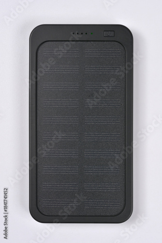 A black, rectangular portable power bank with a segmented solar panel surface and status LEDs is centered on a light gray background
