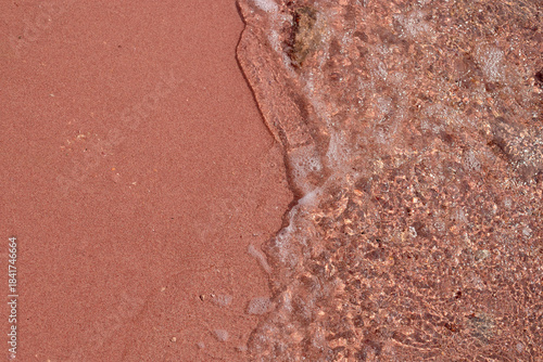 Canvas Print Pink sand beach with gentle waves lapping at the shore creating texture