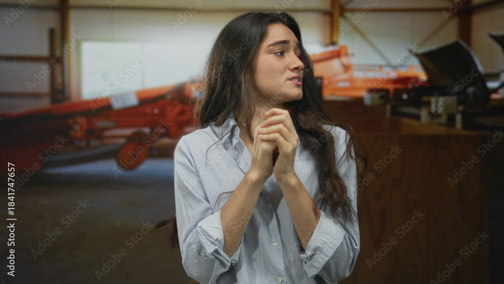 Fototapeta premium Young hispanic woman clasping hands near chest in studio with tense expression; fear vulnerability.