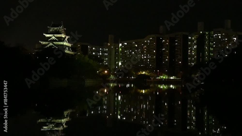 Calm night scene along the water of the illuminated Hiroshima castle and appartments outdoor during the evening with dark sky in Hiroshima city in Japan with space for text.