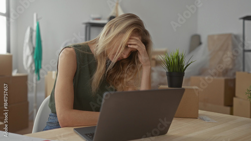 Foto Young woman in new apartment sitting stressed at desk with laptop surrounded by moving boxes, reflecting the challenges of relocation and settling into a new home
