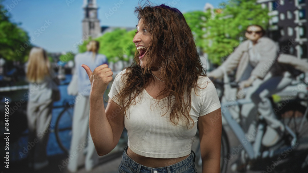 Fototapeta premium Woman giving thumbs up on amsterdam street, smiling with curly hair and pearl necklace, bare midriff visible while standing by canal railing; travel joy adventure.