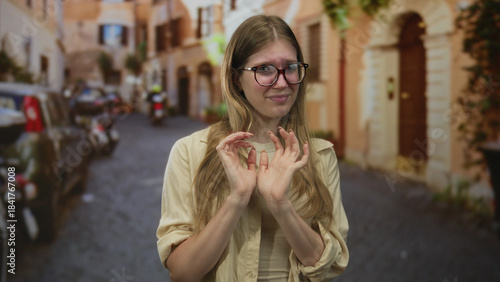 Canvas Print Blonde woman wearing glasses touches fingertips on cobblestone old town street in daylight; uncertainty