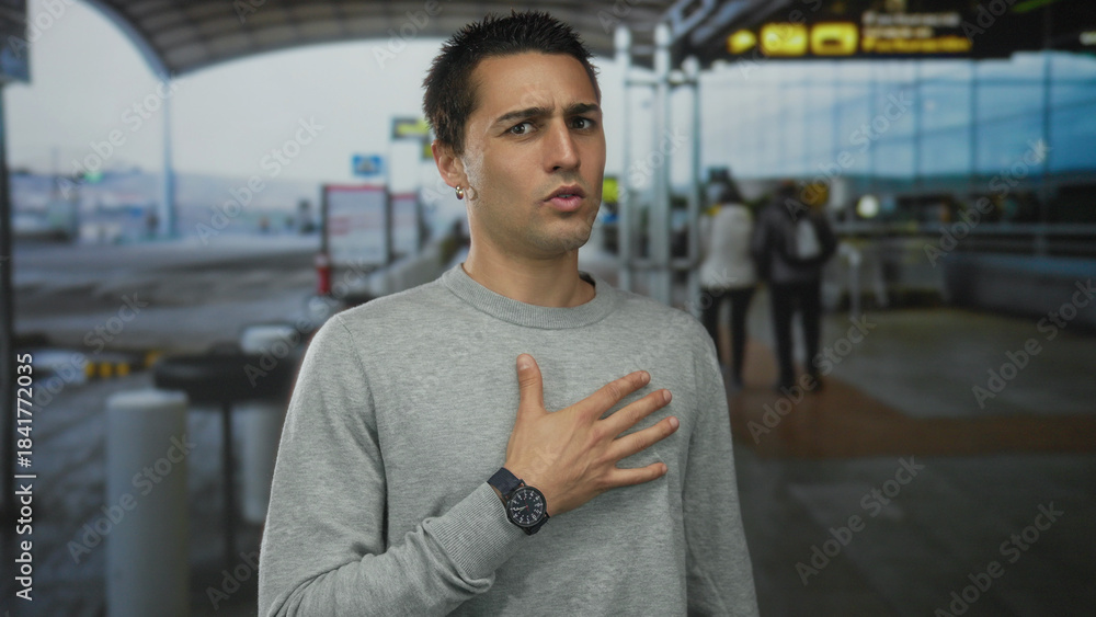 Fototapeta premium Young hispanic man standing outdoors in airport terminal expressing emotions with hand gestures.