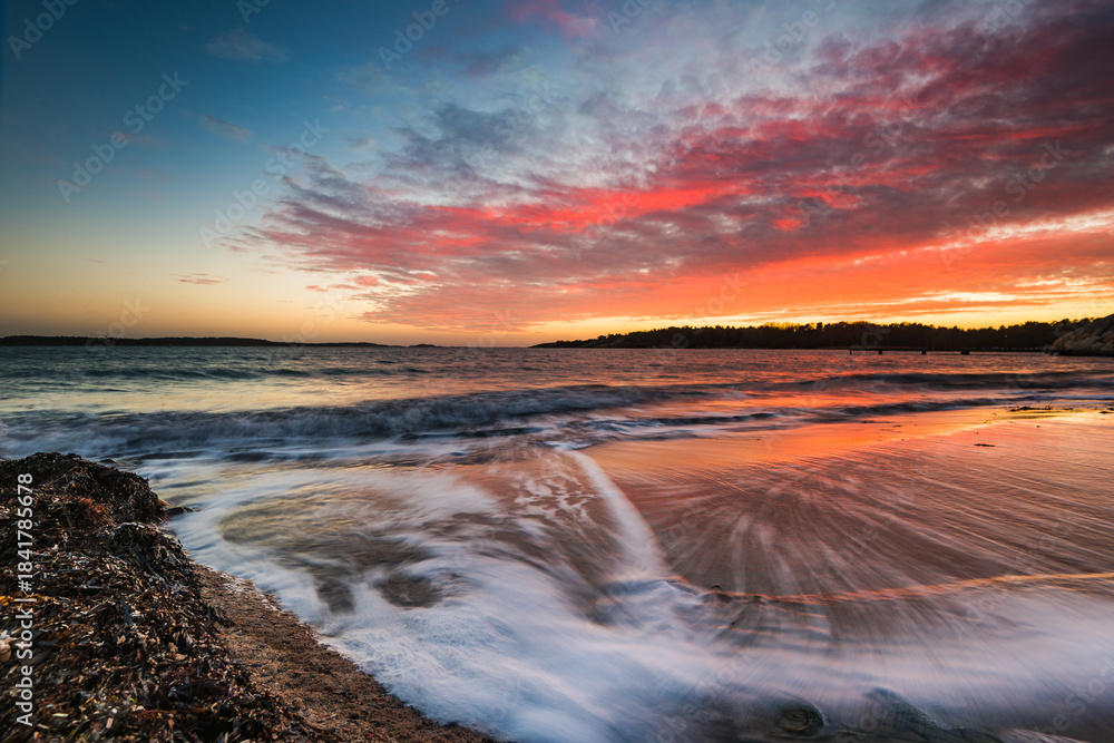 Obraz premium Colorful sunset at beach outside Gothenburg city with waves gently rolling on the shore