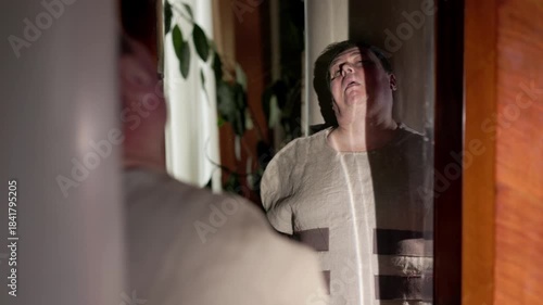 A dim room. A man stares blankly into his own reflection. He is wearing a white straitjacket with long, tied sleeves. The contrast between the motionless body and the inner chaos.