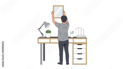 Man hanging a mirror on the wall at his desk, setting up his workspace at home