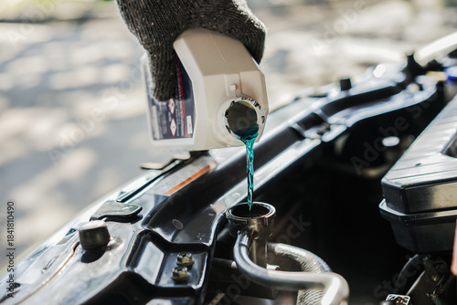  close-up  of a mechanic pouring coolant into the car's radiator for the engine's cooling system. Concepts of car repair and maintenance.