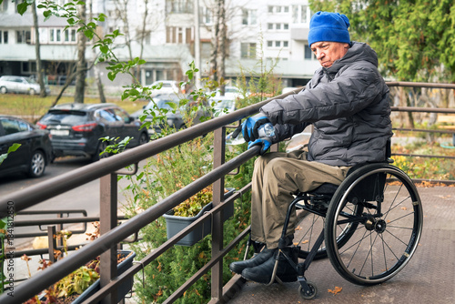 A man in a wheelchair waters flowers on a ramp