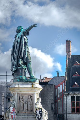Wallpaper Mural Jacob van Artevelde’s bronze statue rises above historic Ghent rooftops, his outstretched arm framed by clouds and architectural details that highlight the city’s medieval heritage. Torontodigital.ca