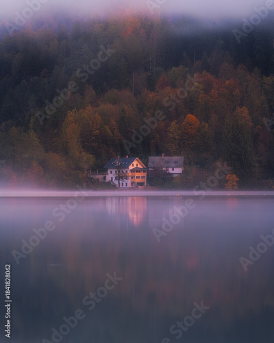 A house by the lake surrounded by autumn colours during a misty sunrise 