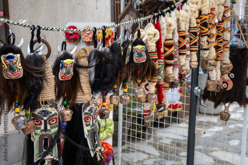 Fototapeta Naklejka Na Ścianę i Meble -  Intricately designed Kukeri masks with animalistic features and decorative wool tassels, adorned with colorful threads and small bells, hung outdoors to scare away evil spirits in Bansko, Bulgaria.