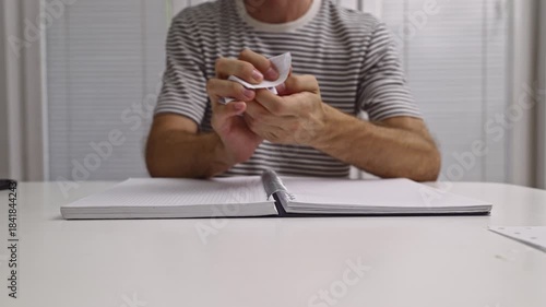 A person tears out a page from a spiral notebook, crumples it into a ball, and discards it on a white desk. This action is repeated, showing frustration or discarding a bad idea.