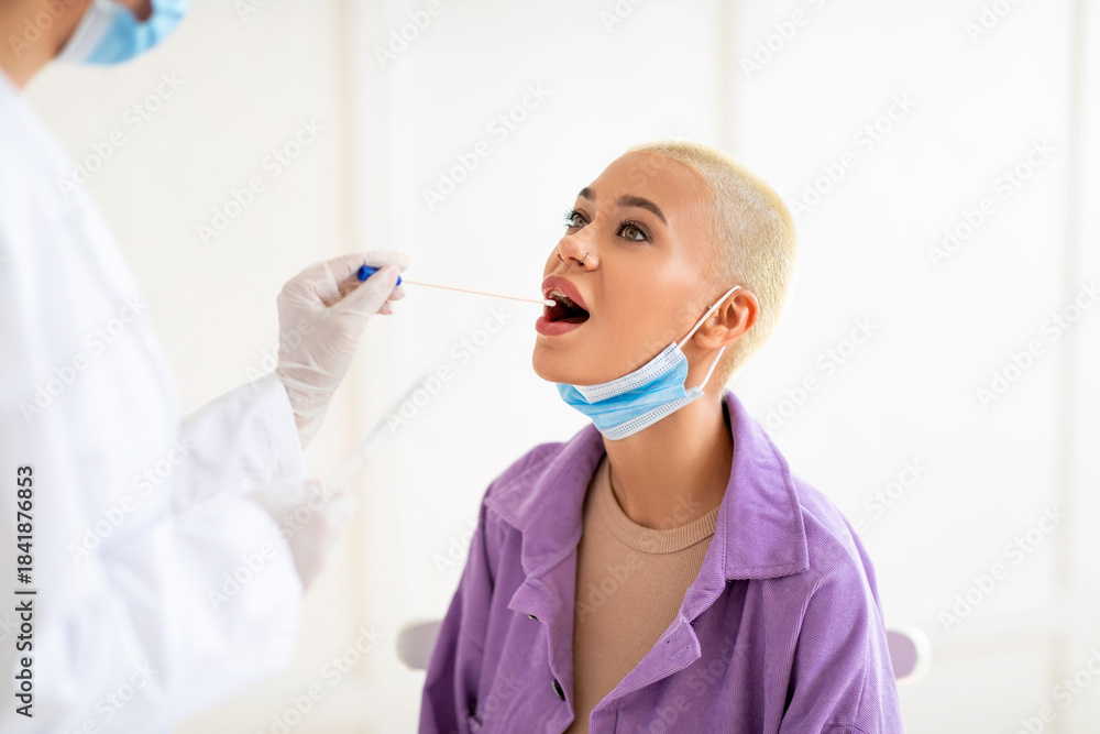 Naklejka premium Millennial lady doing pcr test, getting oral coronavirus swab test, female doctor in protective medical costume making covid-19 swab test from mouth for sick female patient