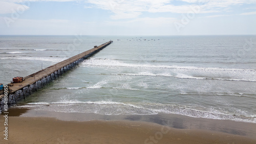 Aerial view of Puerto Eten in Chiclayo, Lambayeque, showing the fishing pier, sandy beach, and calm Pacific coastline under clear skies