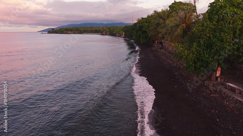 Scenic tropical coastline with dark sand and calm ocean waves at dusk, Indonesia