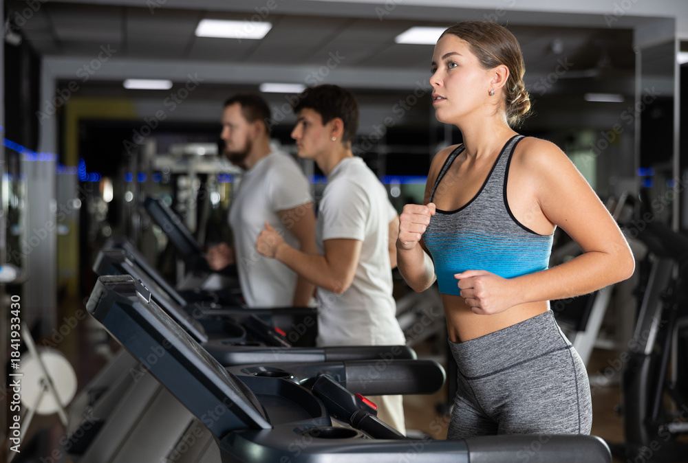 Fototapeta premium Woman runs on a treadmill in the gym. European woman performs cardio zone training