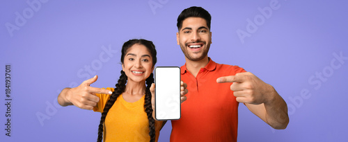 Obraz na plátně Two smiling individuals stand together, pointing at a blank smartphone