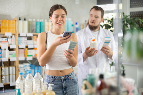 Young woman buyer scanning qr code for moisturizing cream with young man pharmacist in pharmacy